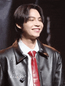 a man wearing a black jacket and a red tie smiles for the camera