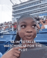 a little girl is sitting in a stadium watching a game and making a funny face .