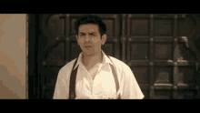 a man in a white shirt and suspenders has a badge on his pocket that says ' a ' on it