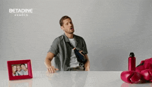 a man is sitting on a table with his legs crossed in front of a picture frame and boxing gloves