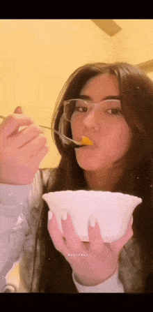 a woman wearing glasses is eating from a bowl