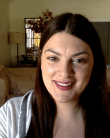 a woman is smiling in front of a couch and mirror