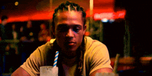 a man with dreadlocks sits at a table with a drink in his hand