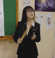 a woman in a suit and glasses is standing in front of a chalkboard holding a book .