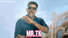 a man wearing sunglasses says mr.tk in front of buildings