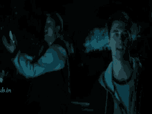 two men are standing next to each other in the dark and one of them is holding something in his hand .