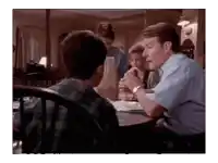 a man is sitting at a table talking to a young boy