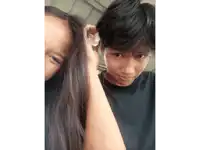 a boy and a girl are standing next to each other and the girl is touching the boy 's hair