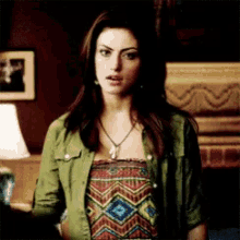 a woman is wearing a green jacket and a necklace while standing in a room .