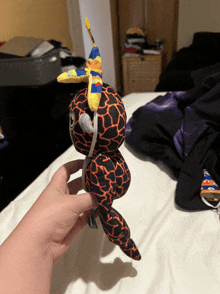 a person is holding a stuffed animal that looks like a giraffe with a blue and yellow feather on its head