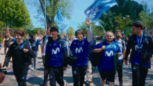 a group of people wearing blue shirts with the letter m on them walk down a street