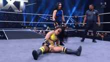a female wrestler is laying on the ground in a wrestling ring while another wrestler stands behind her