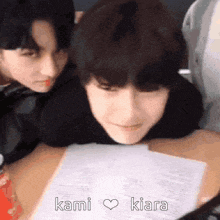 two young men are sitting at a table with a piece of paper and the words kami kiara written on it