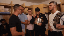 a group of men are standing in a locker room and one of them is holding a championship belt