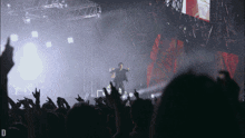 a man stands on a stage in front of a crowd with the letter d in the lower right corner