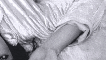 a black and white photo of a woman laying on a bed with a white shirt on