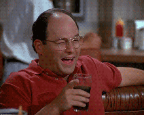 a bald man with glasses is holding a glass of soda and laughing .