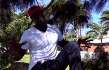 a man wearing a white shirt and a red hat is sitting on a tree branch
