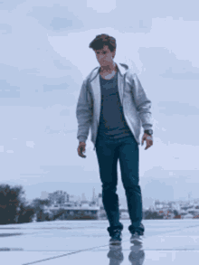 a young man in a grey jacket and blue jeans is standing on a skateboard