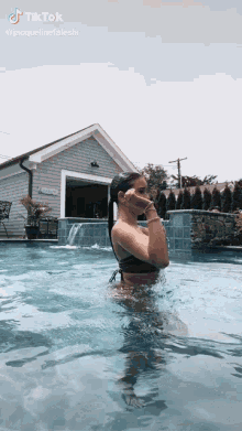 a woman in a bikini is standing in a swimming pool with a waterfall .