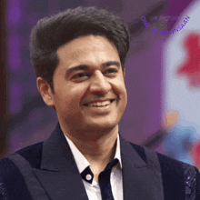 a man in a suit and tie is smiling with a gif factory logo behind him