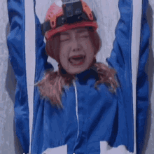 a woman wearing a blue jacket and a red helmet is crying with her eyes closed
