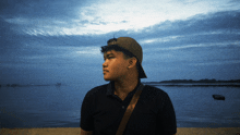 a man wearing a baseball cap stands in front of the ocean
