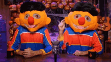 two men dressed as sesame street characters are sitting at a table with a microphone .