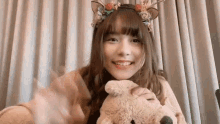 a young woman wearing a reindeer headband is holding a teddy bear and smiling .