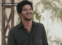 a man in a black shirt is smiling while standing in front of a building .