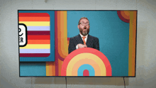 a man in a suit and tie is giving a speech in front of a colorful background with the letter r on it