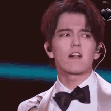 a young man wearing a bow tie and ear buds is making a funny face .