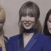 a woman wearing a blue jacket and choker is smiling while standing next to two other women .