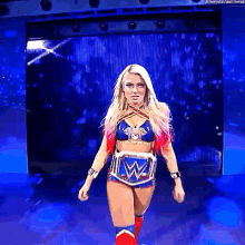 a woman in a wrestling outfit is walking on a stage in front of a blue screen .