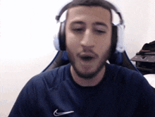 a man wearing headphones and a nike shirt is making a funny face while sitting in a chair .