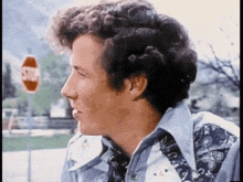 a man with curly hair is standing in front of a stop sign and looking at something .
