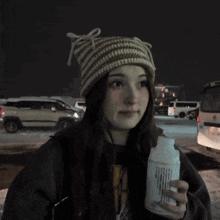 a woman wearing a knitted hat is holding a bottle of something