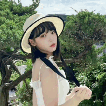 a girl wearing a hat and a white dress stands in front of a tree