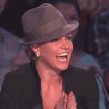 a woman wearing a hat and a black jacket is laughing while speaking into a microphone .