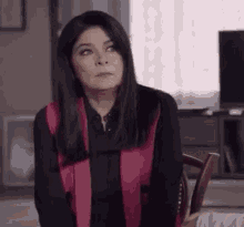 a woman is sitting in a chair in a living room wearing a black shirt and a pink scarf .