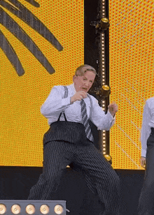 a man in a suit and tie is dancing on a stage in front of a yellow screen .
