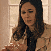 a woman in a trench coat is holding a small glass object