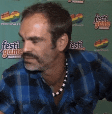 a man wearing a blue plaid shirt is standing in front of a green wall that says " festi game "