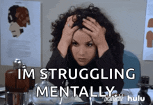 a woman with curly hair is sitting at a desk with her hands on her head and the words im struggling mentally