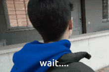 a person wearing a blue hoodie says wait on their back