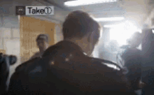 a man is standing in a room with a sign that says take on it