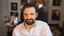 a man with a beard is sitting in a chair in front of a wall with pictures