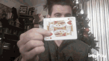 a man is holding a playing card in front of his face with a christmas tree behind him