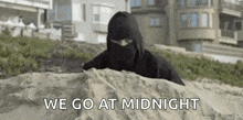 a man in a ninja costume is hiding in the sand .