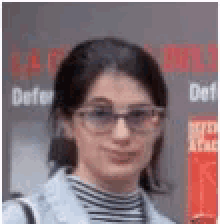 a woman wearing sunglasses and a striped shirt is standing in front of a sign .